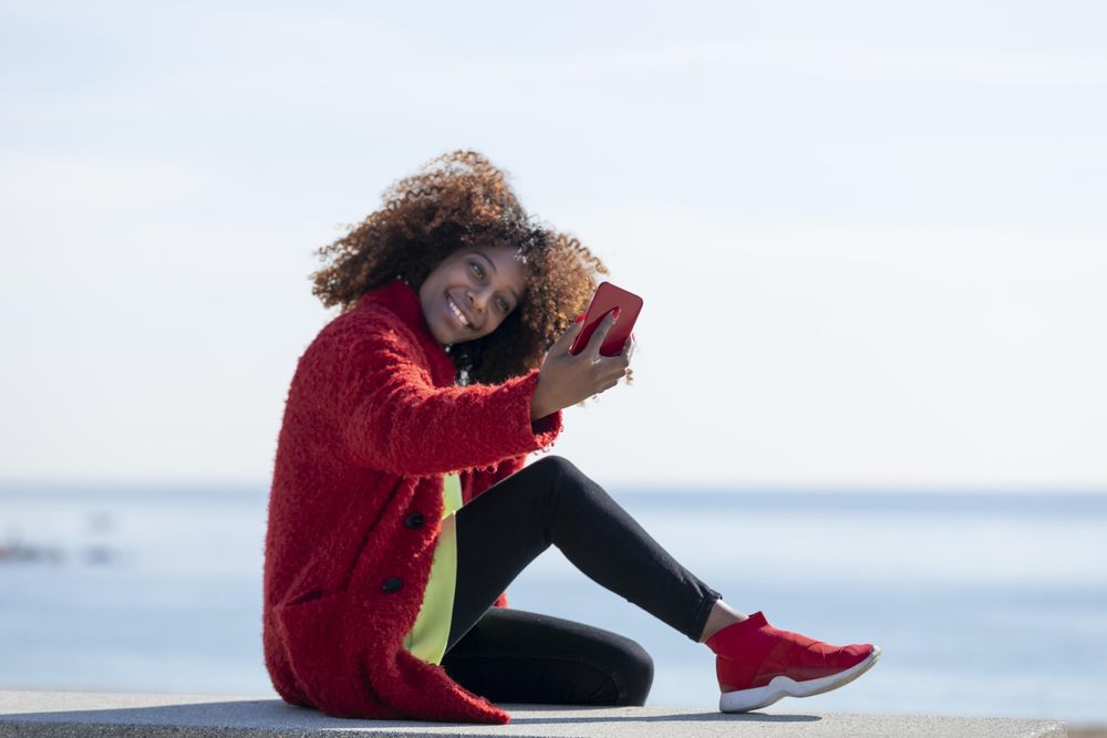 Side view of female taking picture on smart phone on bench on the beach
