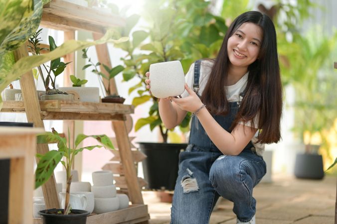 Asian female gardener deciding what pot to use at work