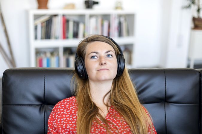 Blonde young woman listening to music on headphones while relaxing on sofa