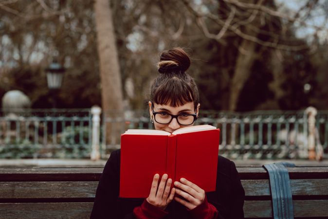 Young woman reading book on bench in park