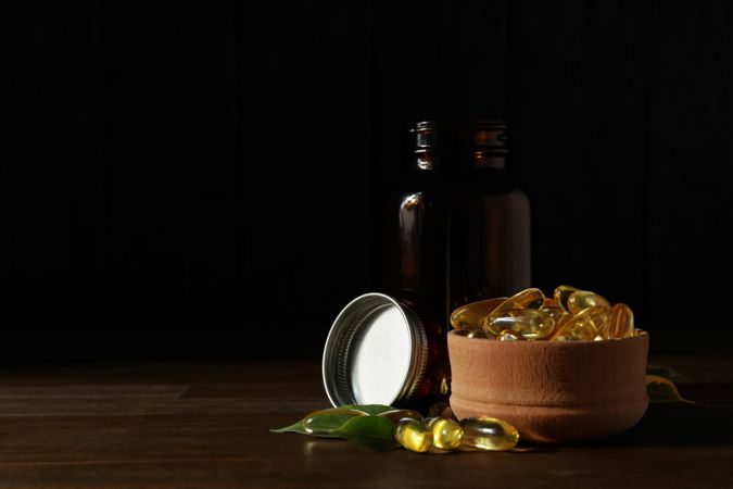 Wooden bowl with omega pills on dark background