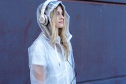 Pensive stylish woman in raincoat with headphones