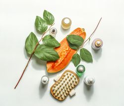 Body care cosmetic setting with halved papaya, beauty products, dry massage brush and green leaves. Sustainable beauty skin care concept. Top view.