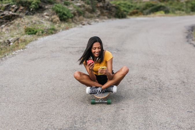 Latina cheerful woman with crossed legs riding longboards