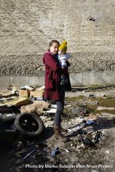 Woman holding her baby looking at rubble, vertical bDzNK5