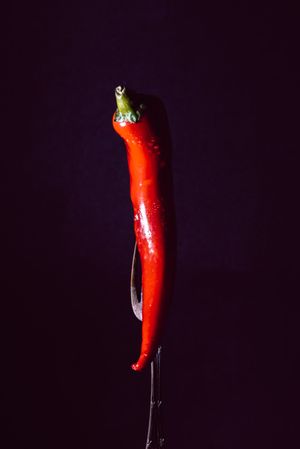 red chili pepper on fire in fork on a dark background