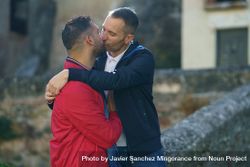 Two males hugging each other near stone wall outside bGkPYb