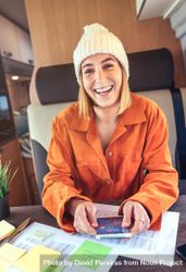 Woman in orange shirt sitting and laughing in van with smartphone, vertical 0g1Dl4