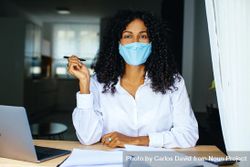 Confident woman holding a pen and working on documents while wearing a facemask bD8VVb