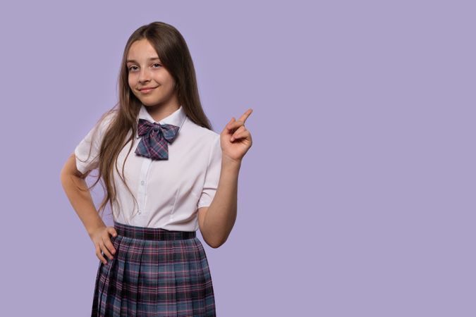 Girl in white shirt and plaid skirt pointing upwards