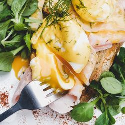 Eggs Benedict with yoke broken with greens, coffee, top view, close up, square crop