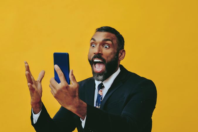 Energetic Black businessman in suit yelling at smartphone screen
