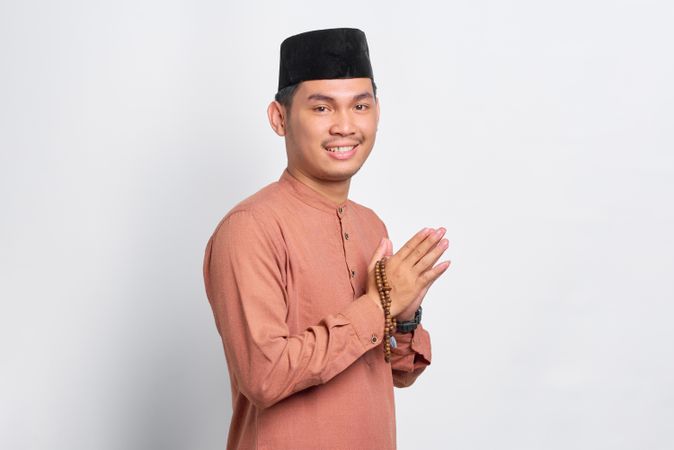 Smiling Muslim man in kufi head wear with his hands pressed together in prayer