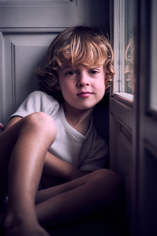 Tranquil little kid sitting near window and looking at camera
