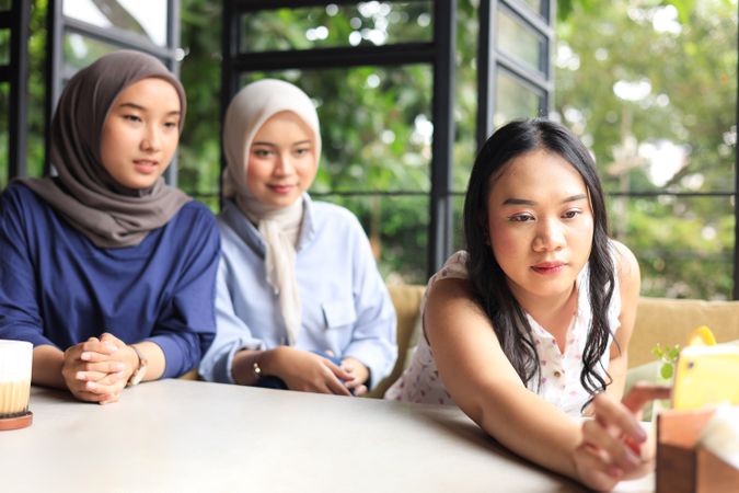 Three Asian Female Friends Happy Sitting in Cafe Next to Window doing Internet Trend Challenge