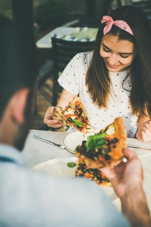 Couple eating pizza al fresco with wine, woman looking down smiling