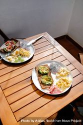 Casual breakfast table set in the sun with eggs, fresh fruit, and avocado toast 47gJl4