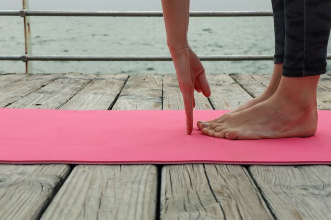 Female hands and feet on pink yoga mat on wooden floor outdoors, close up