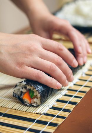 Hands of chef securing freshly made sushi rolls