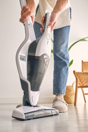 Anonymous woman removing container from modern upright vacuum cleaner