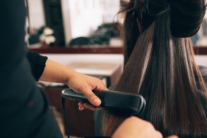 Hairdresser using hair straightener to straighten woman’s hair