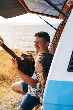 Amorous man plying on guitar and looking at woman in trunk of car
