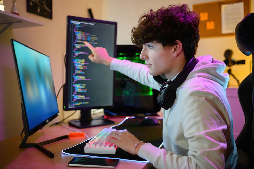 Concentrated young man sitting at table and working on computer in gaming room