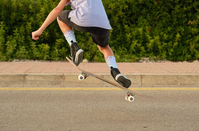 Crop boy jumping with skateboard and showing trick