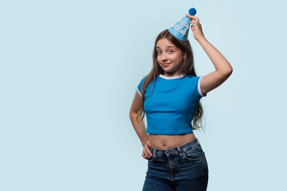 Girl adjusting birthday hat, showing playful and confident expression.