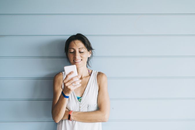 Smiling adult woman leaning on a wood wall while using a smartphone