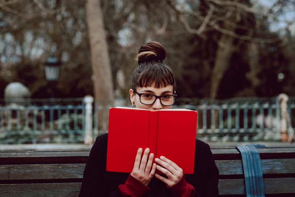 Young woman reading book on bench in park