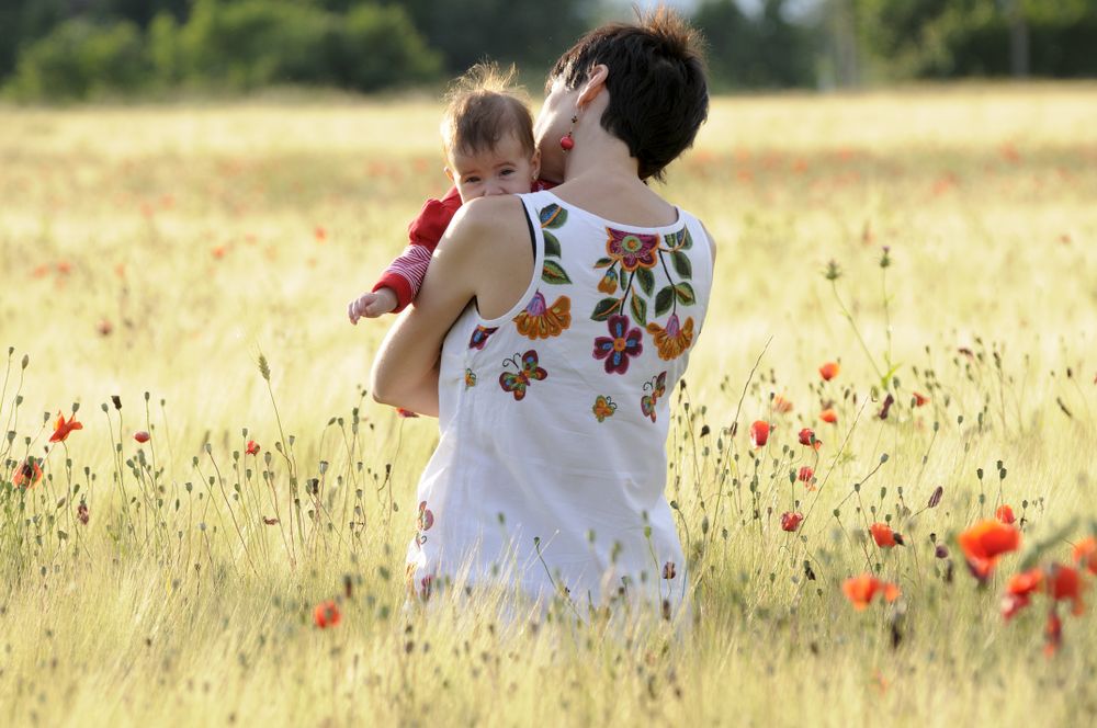 Back of mother holding her cute daughter in field