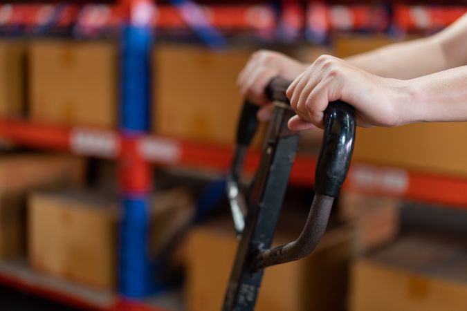 Close up hand of staff worker pushing trolley or picking cart in warehouse store