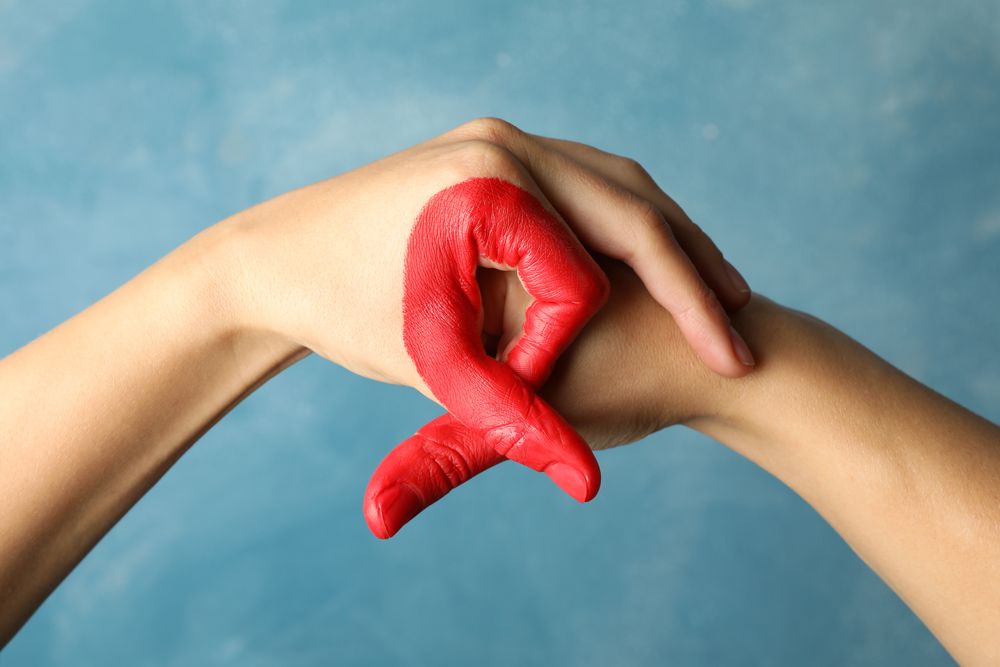 Two hands depict AIDS awareness sign against blue background, close up