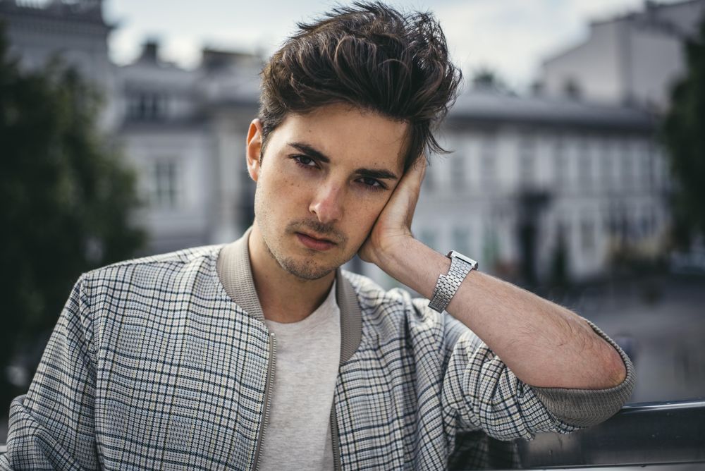Man wears grey plaid jacket leaning his head on his hand outdoor