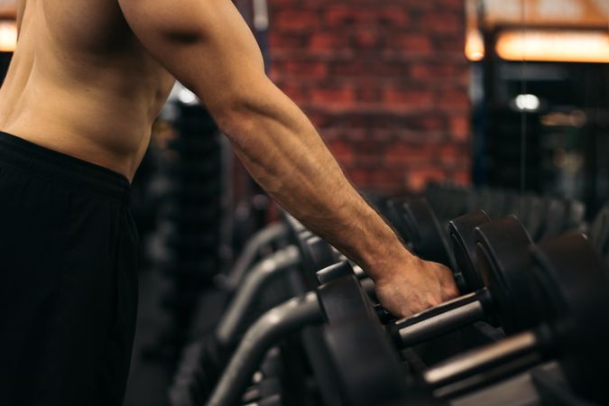 shirtless strong man lifting dumbbell in a gym