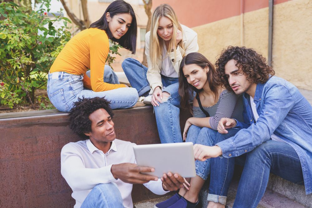 Male and female friends gathered around a digital tablet outside