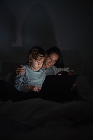 Woman with son using laptop while doing homework in darkness