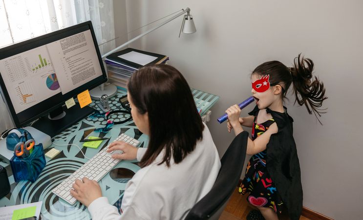Woman working from home with her daughter singing by her side