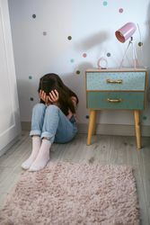 Unrecognizable little girl covering her face with hands sitting on the floor