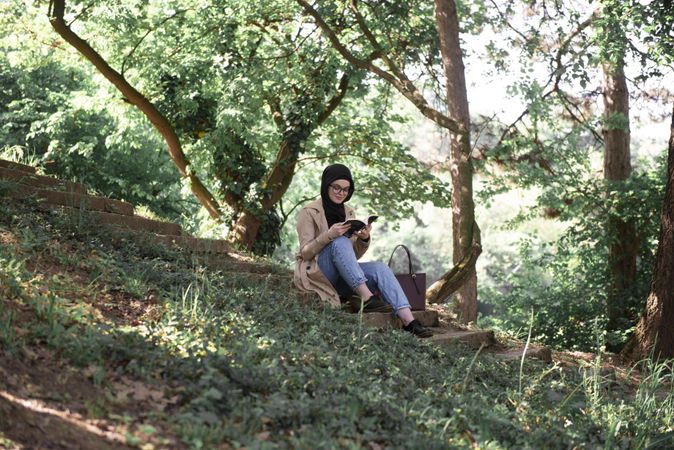 Middle Eastern woman sitting on hill reading book