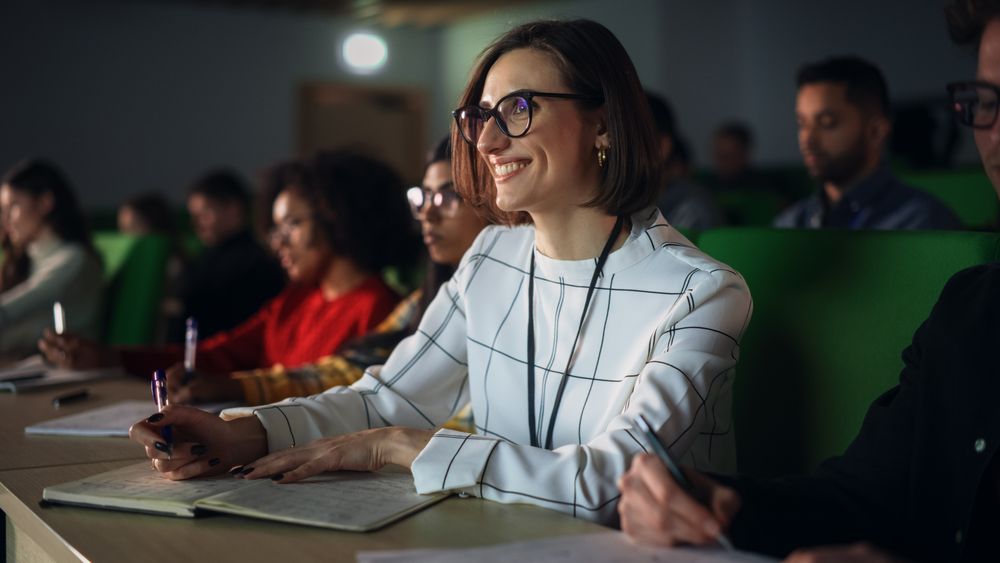 Thoughtful Young Female Studying in University, Listening to a Lecture in a Crowded Room