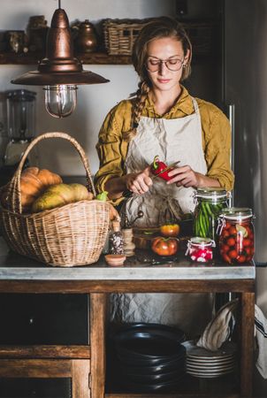 Young woman in glasses in rustic kitchen cutting pepper