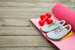 Karemat, sneakers and dumbbells on wooden background, space for text