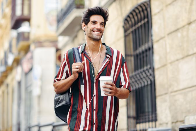 Male in striped shirt walking through the streets of Granada, Spain with coffee