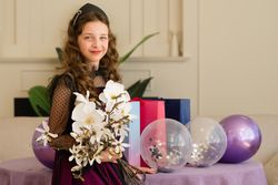 Girl holding flowers and balloons at birthday celebration.