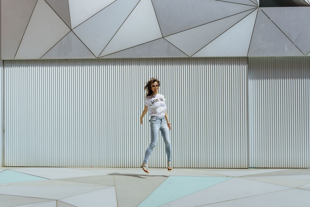 Cheerful woman jumping near modern wall