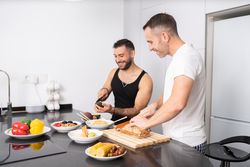 Smiling male couple preparing vegetables and cutting bread for lunch