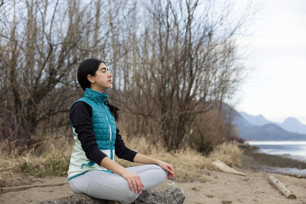 Young female with her eyes closed sitting on a log while meditating