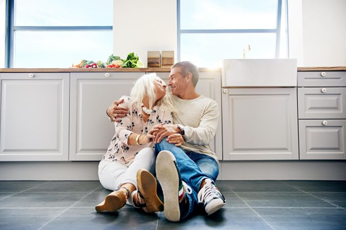 Older couple embracing and looking at each other on floor of bright kitchen